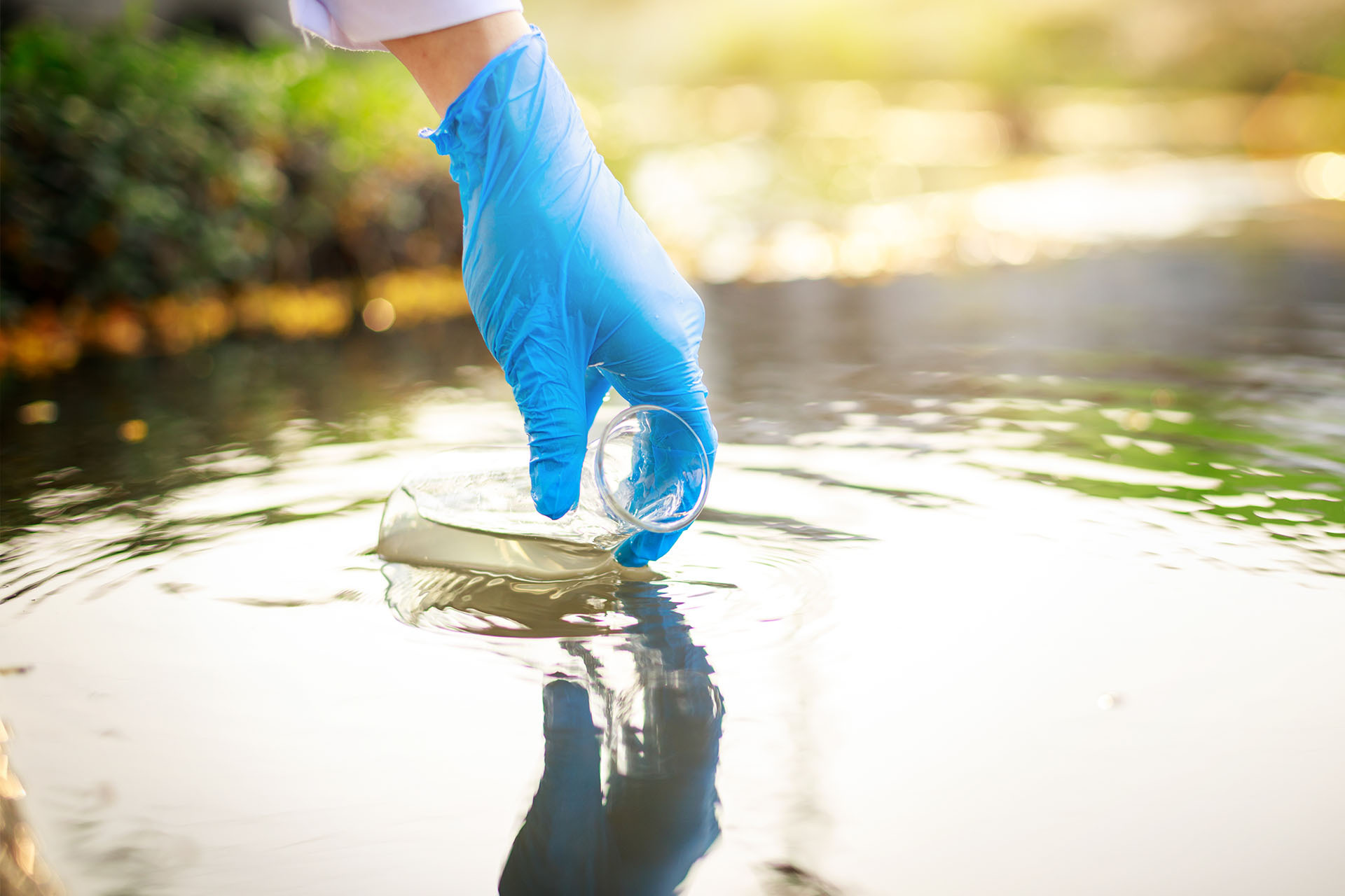 Ein Mitarbeiter verwendet einen Erlenmeyerkolben, um eine Probe aus dem Abwasser zu entnehmen, um diese anschließend zu analysieren.